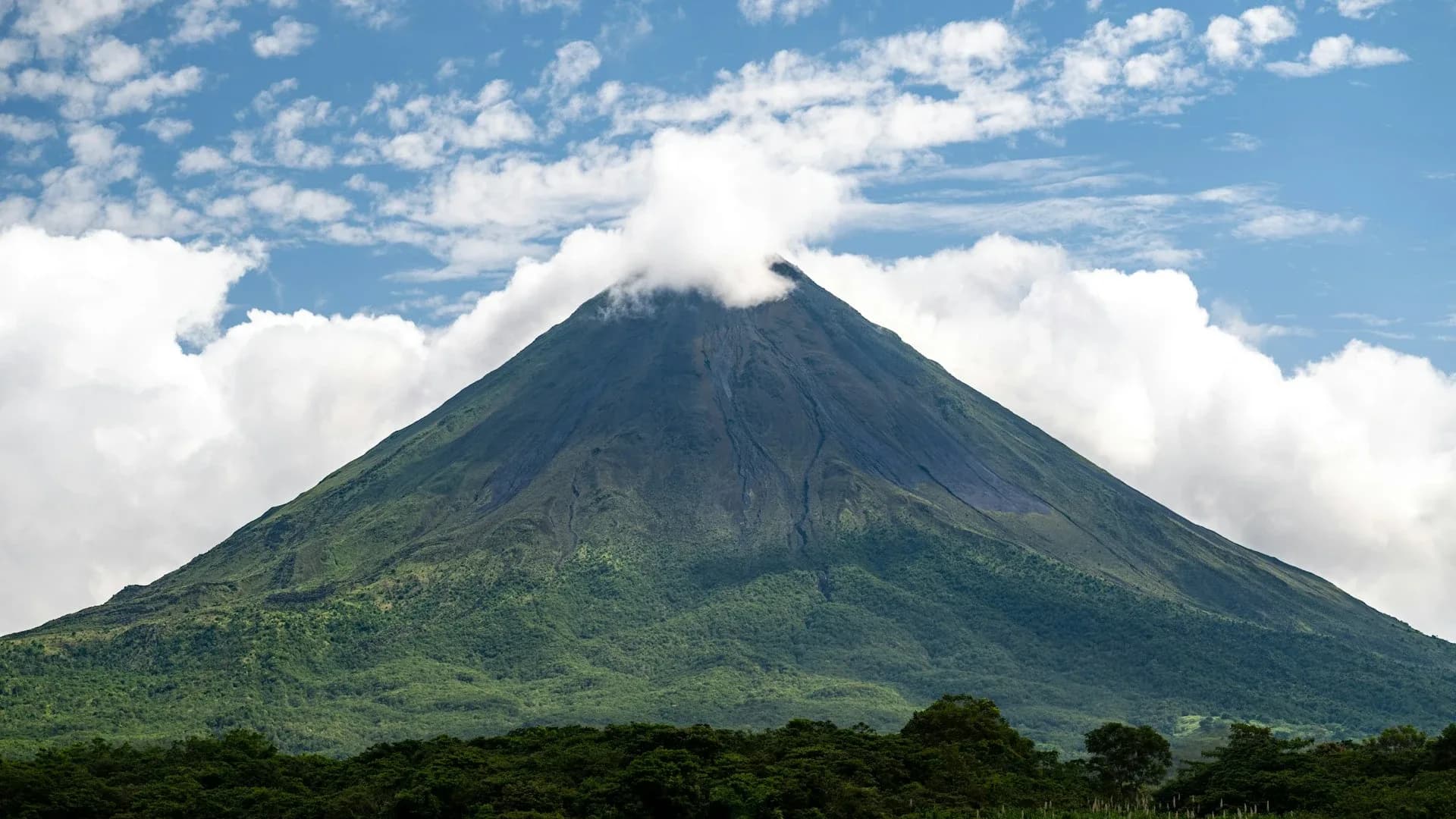 El Volcán Arenal sobre el bosque lluvioso entre nubes de la mañana, destino de los tours de un día desde Guanacaste, Costa Rica