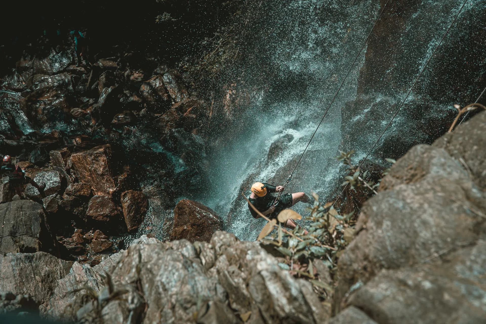 Person rappelling down a tall jungle waterfall on a canyoning tour in the rainforest near Arenal Volcano, La Fortuna
