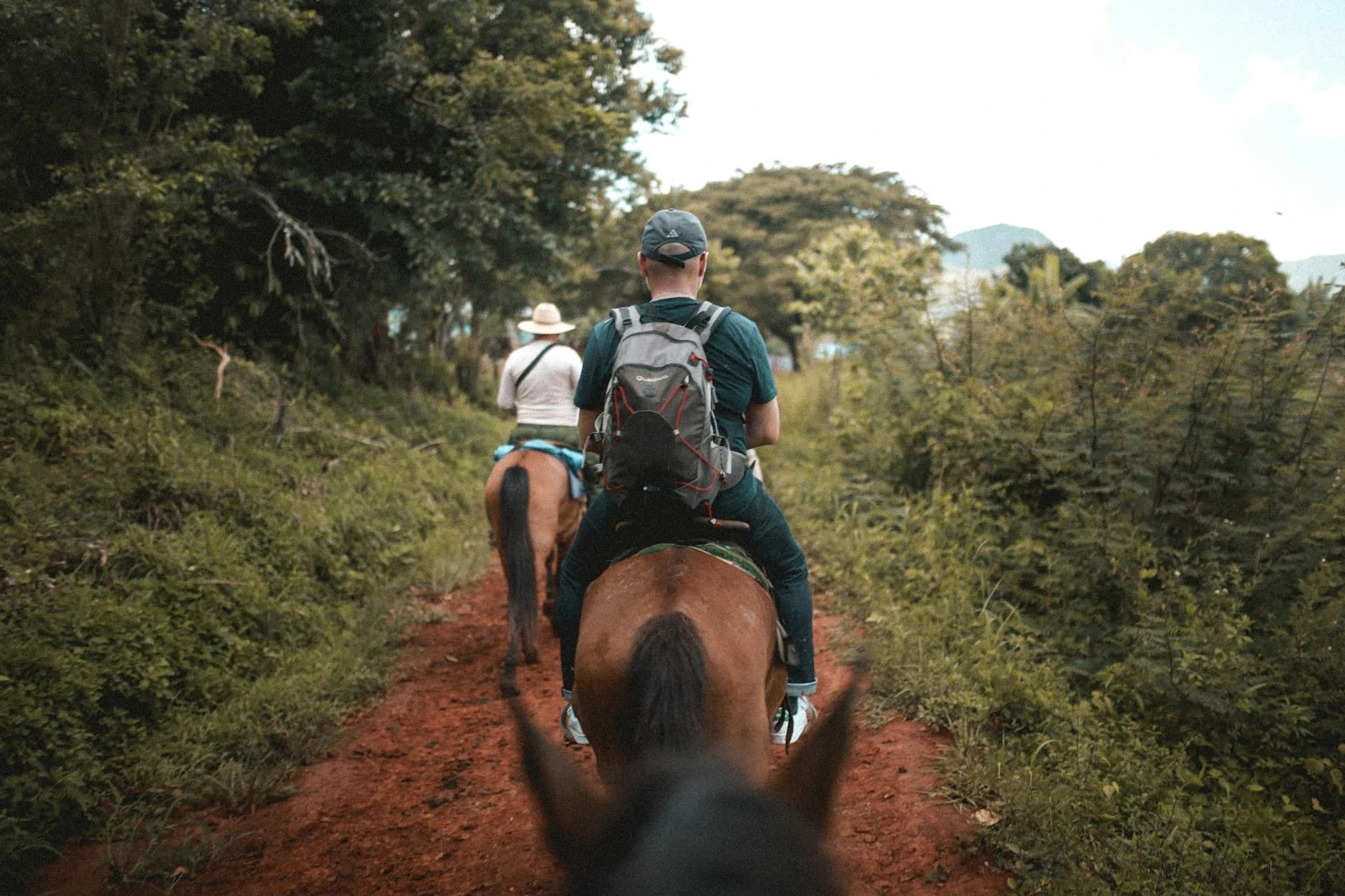 Riders on horseback crossing green pastureland with the Arenal Volcano rising in the background near La Fortuna