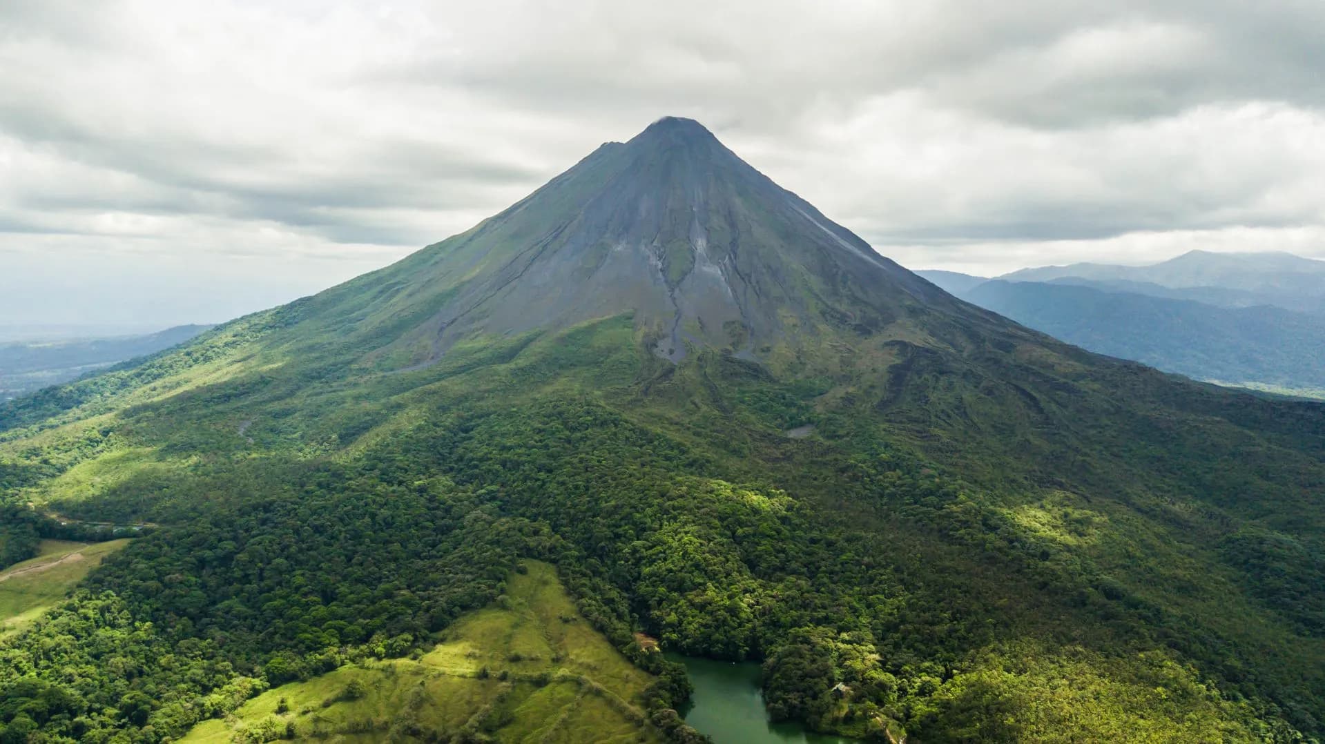 Arenal Volcano cone emerging above green rainforest on a bright early-December morning in La Fortuna, Costa Rica