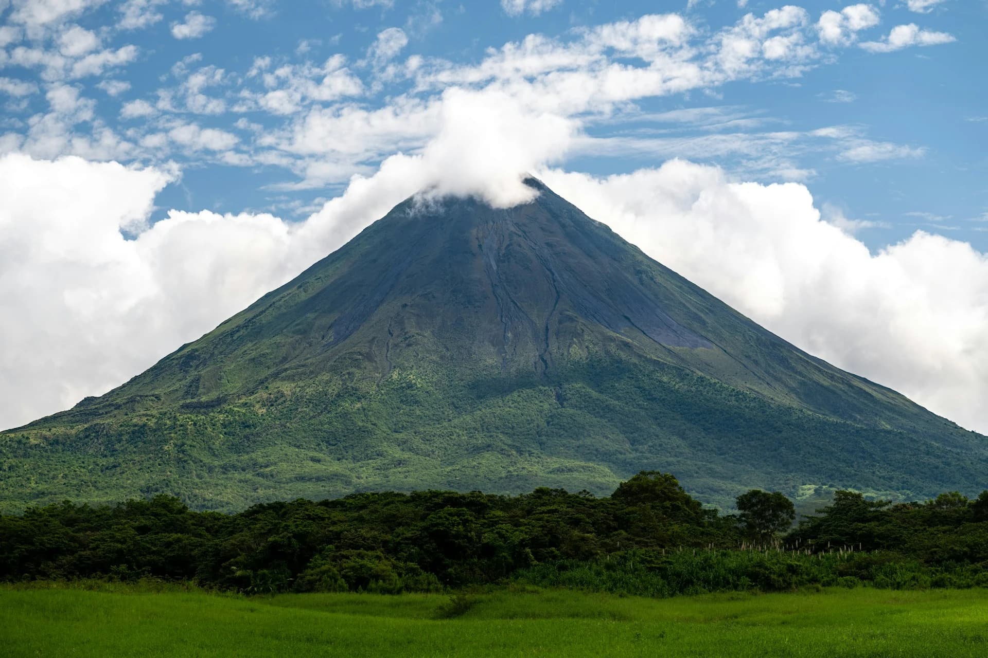 Split view of the Arenal Volcano under clear dry-season skies and wrapped in green-season cloud above the rainforest near La Fortuna, Costa Rica
