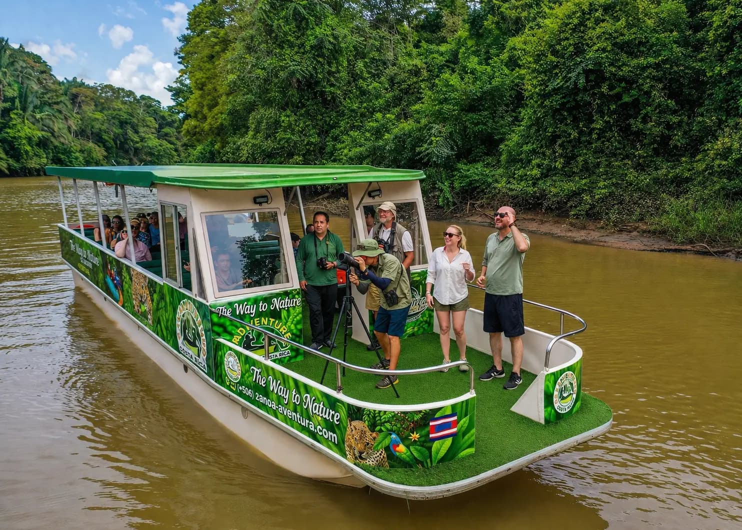 Guided safari float boat drifting past rainforest riverbank with a sloth and herons near La Fortuna, Costa Rica
