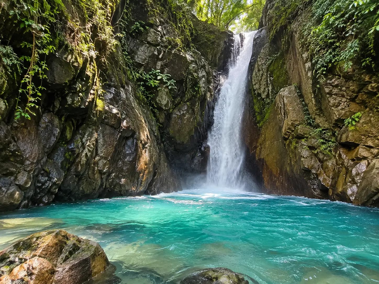 Blue waterfall falling into a narrow orange canyon at La Leona, Curubande, Guanacaste, Costa Rica