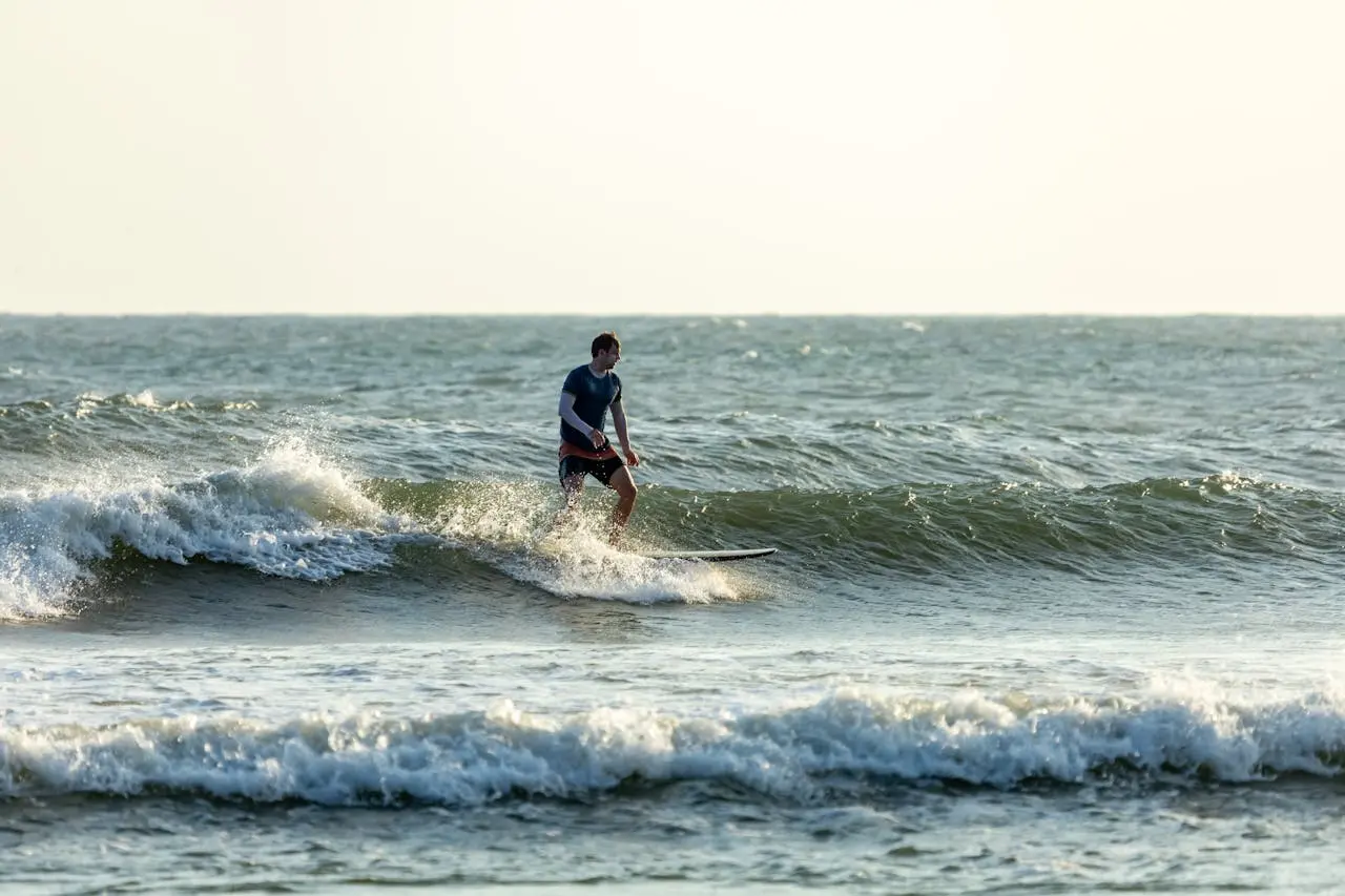 Beginner surfer catching a wave at Playa Tamarindo with a palm-fringed Guanacaste coastline in the background