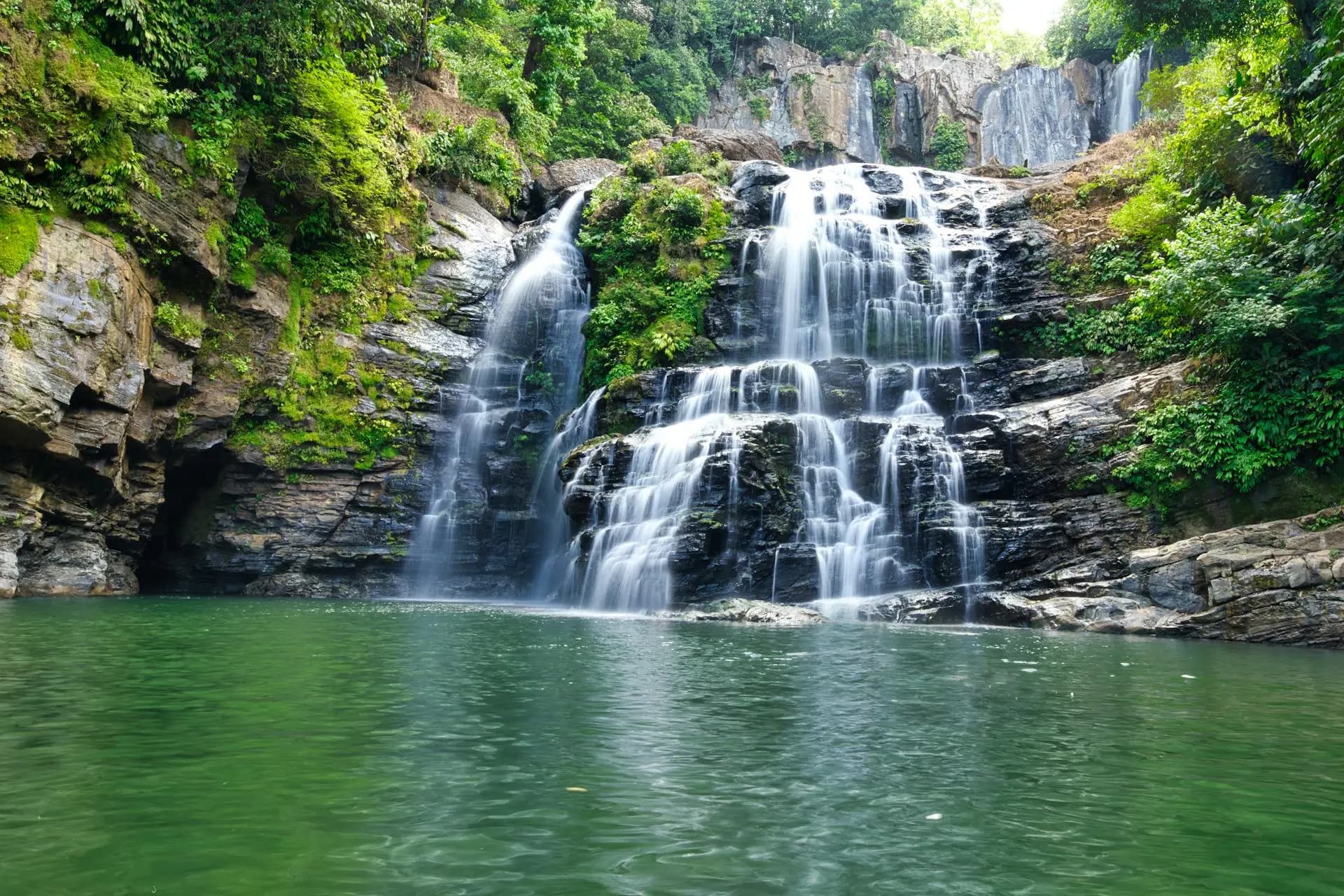 Swimmer at the base of the tall Nauyaca waterfall surrounded by lush tropical jungle near Manuel Antonio, Costa Rica