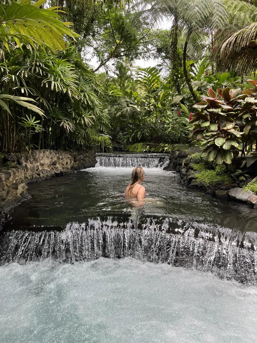 Solo swimmer in a natural hot spring river surrounded by rainforest at Tabacón Hot Springs Resort, La Fortuna
